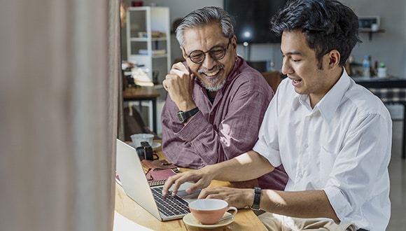 Father and son sitting at a laptop discussing health cover